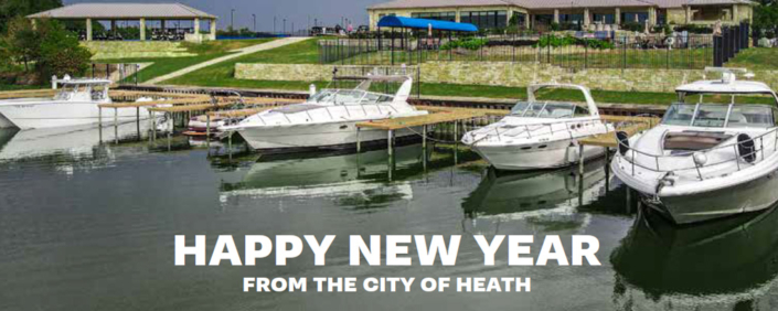 0226 Several white motorboats docked at a marina on calm water, with grassy terraces and buildings in the background. Large white text across the bottom reads, ‘HAPPY NEW YEAR FROM THE CITY OF HEATH.