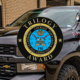 Black police pickup truck parked outside a brick building, marked “City of Heath Police,” with emergency lights and a fire truck visible in the background; an FBI “Trilogy Award” emblem is overlaid prominently in the center of the image.