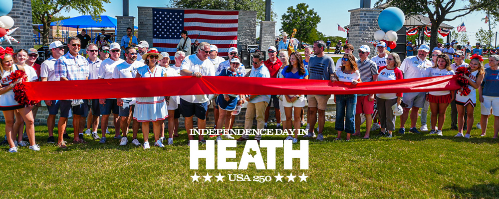 Community members gather for a ribbon-cutting ceremony celebrating the newly renovated Towne Center Park in Heath, Texas, during the city's Independence Day festivities. A large American flag hangs in the background as officials and residents stand behind a wide red ribbon, with patriotic decorations, balloons, and cheerleaders on either side. The image includes the text: "Independence Day in Heath – USA 250.