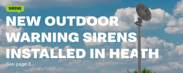 0925 An outdoor warning siren in the foreground with a blue sky featuring white fluffy clouds.