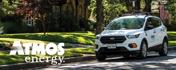 A white SUV driving in a suburban neighborhood with an Atmos Energy logo on the side of the vehicle.