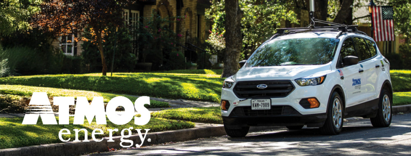 A white SUV driving in a suburban neighborhood with an Atmos Energy logo on the side of the vehicle.