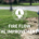 A silver fire hydrant with blue caps stands beside a grassy roadside in a suburban neighborhood,.