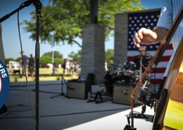 Musicians perform on stage at the amphitheater in Towne Center Park in Heath, Texas, during an outdoor community celebration. A close-up of an upright bass is shown in the foreground, with a drummer, microphone stands, and an American flag visible on stage. A "Music Friendly Texas – Heath" logo appears in the lower-left corner.