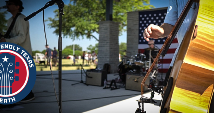 Musicians perform on stage at the amphitheater in Towne Center Park in Heath, Texas, during an outdoor community celebration. A close-up of an upright bass is shown in the foreground, with a drummer, microphone stands, and an American flag visible on stage. A "Music Friendly Texas – Heath" logo appears in the lower-left corner.