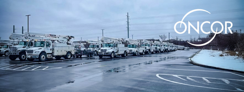 A long row of white Oncor utility bucket trucks parked in a wet lot on an overcast winter day, with patches of snow along the edges and the Oncor logo displayed in the upper right.
