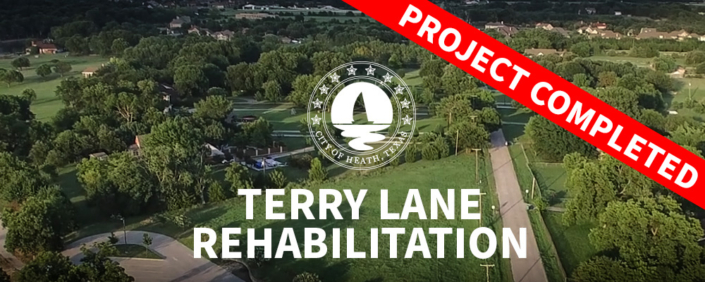 An aerial view of a lush, green residential neighborhood featuring scattered houses and roads. Superimposed in the center is the white circular seal for the City of Heath, Texas, which includes a sailboat motif surrounded by stars. Below the seal, large white text reads "TERRY LANE REHABILITATION". A prominent red diagonal banner stretches across the top right corner with bold white text that says "PROJECT COMPLETED".