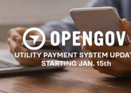 Banner announcing an OpenGov utility payment system update starting January 15, showing a person holding a smartphone next to a laptop on a desk.