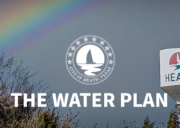 A colorful rainbow in a dark grey sky with the Heath South water tower in the foreground.